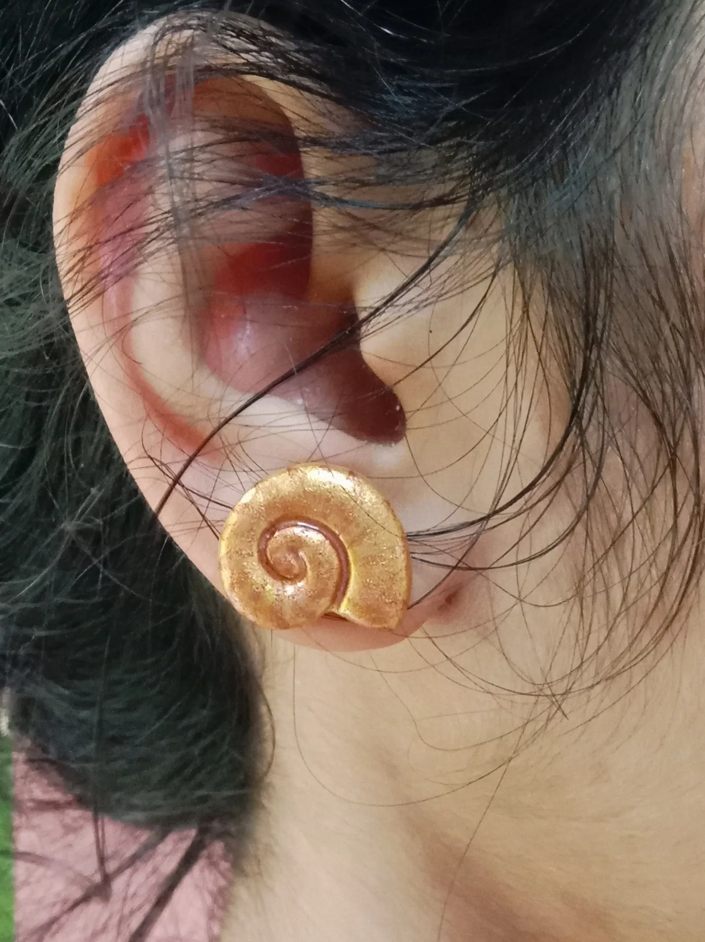 Close up of a woman wearing the lightweight golden clay spiral shell stud earring for everyday style.