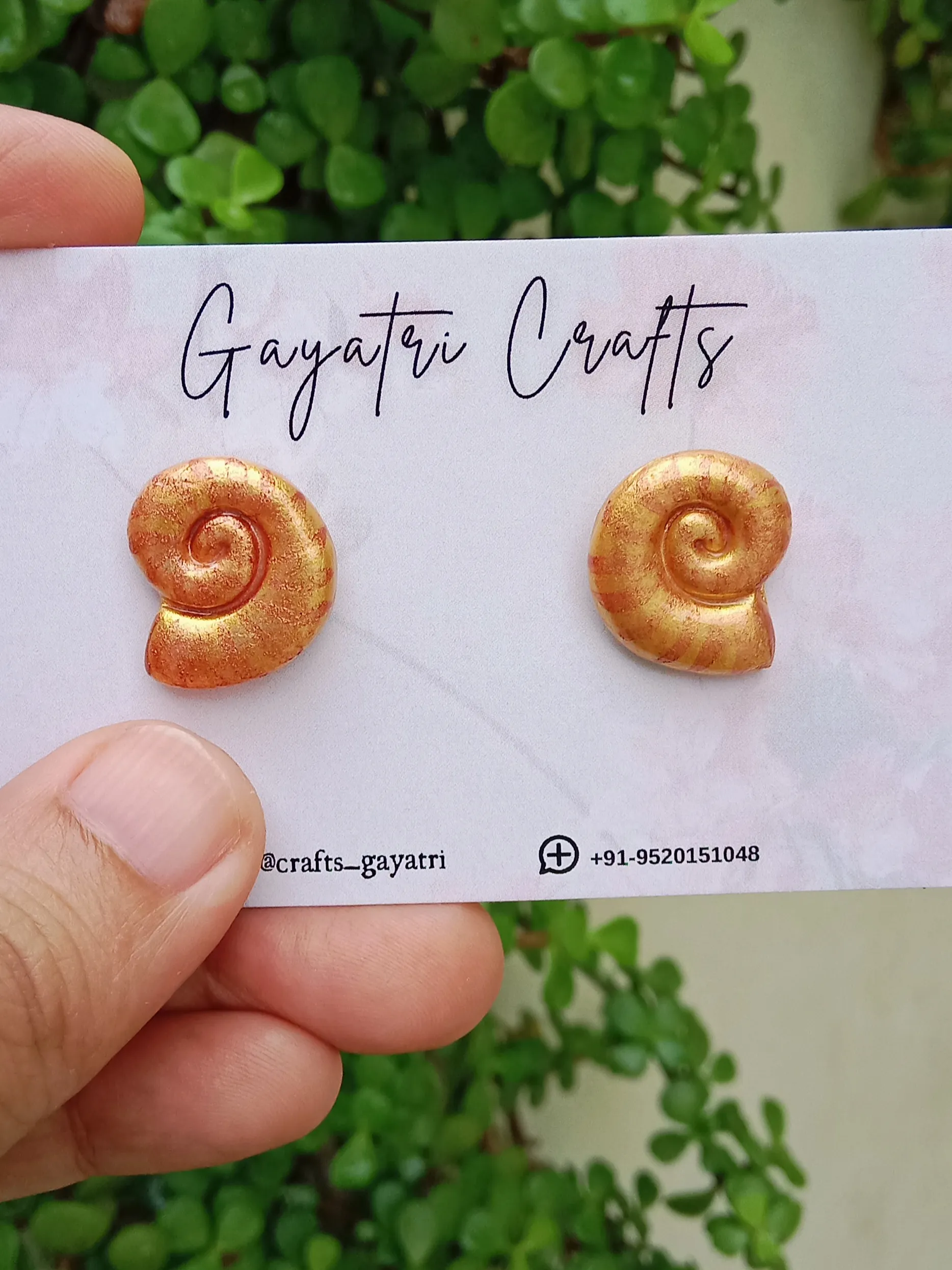 Front view of Studio Gayatri handmade golden spiral shell clay stud earrings on a clean background