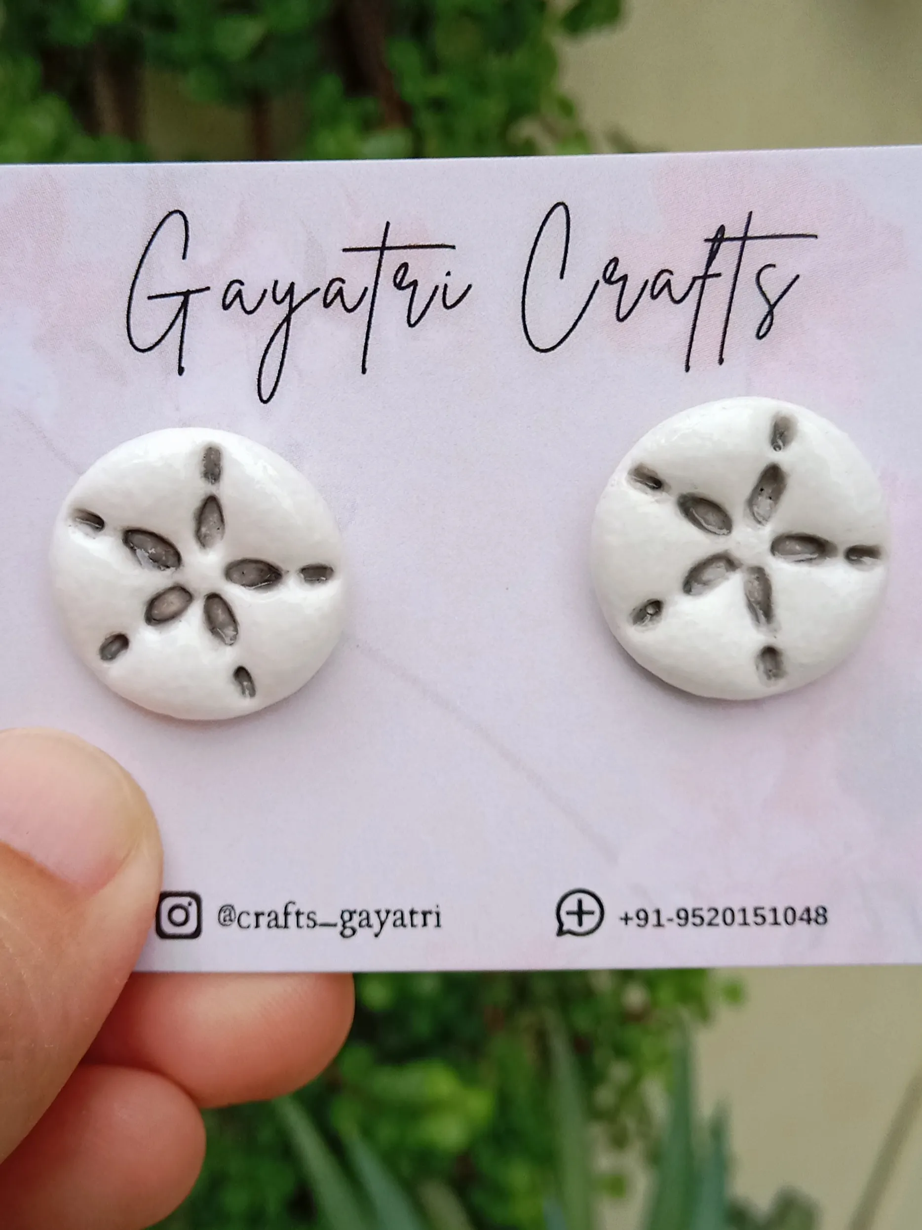 Front view of Studio Gayatri handmade pure white round clay stud earrings with a black engraved starfish ceramic look design.