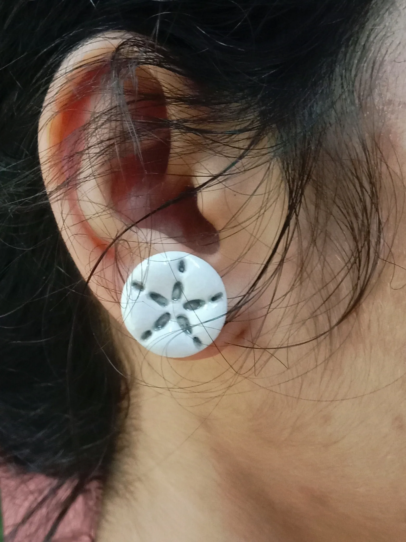 Close up of a woman wearing the minimalist small and lightweight white starfish clay stud earring for daily styling.