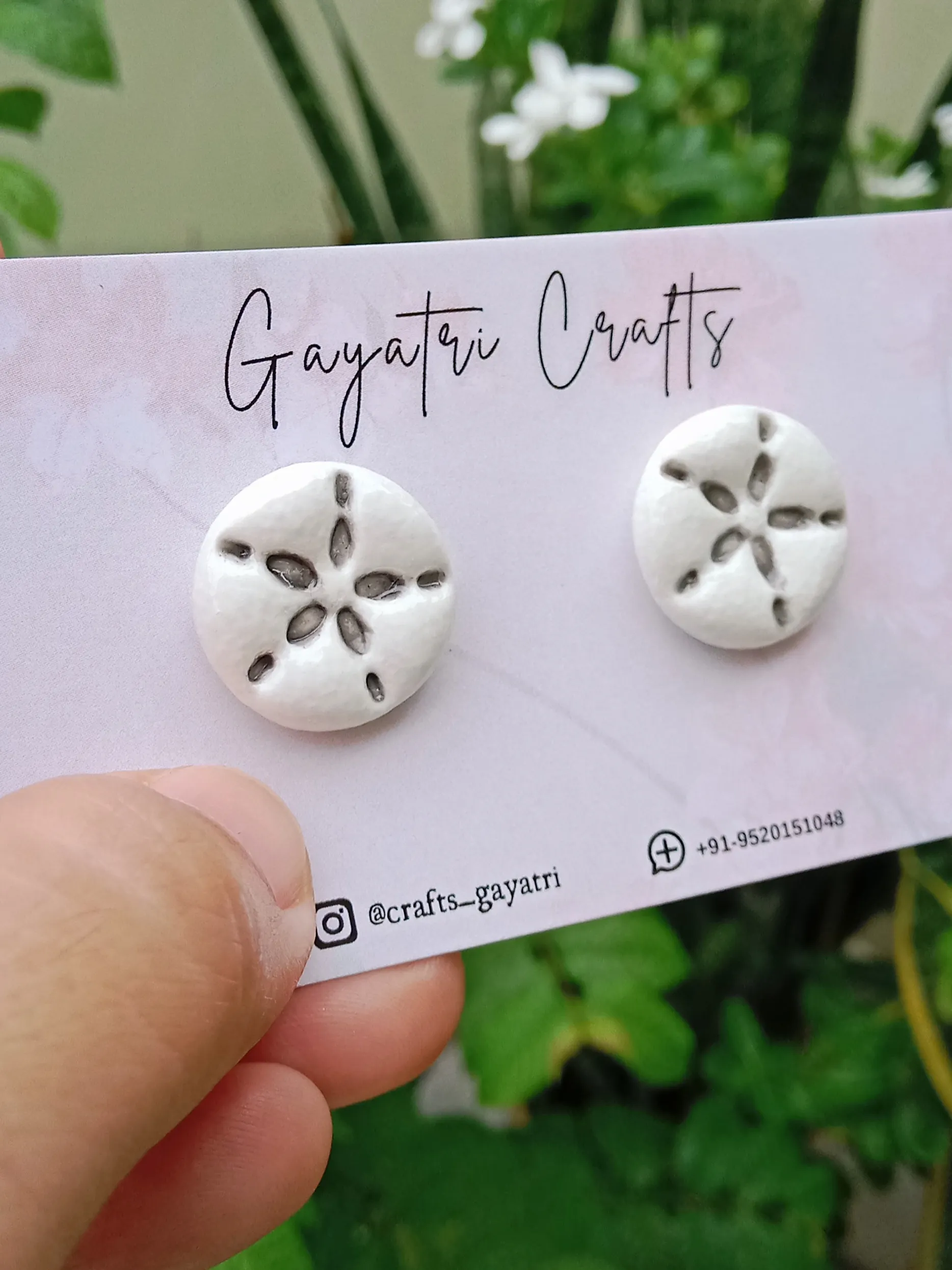 Side view of Studio Gayatri handmade pure white round clay stud earrings with a black engraved starfish ceramic look design.
